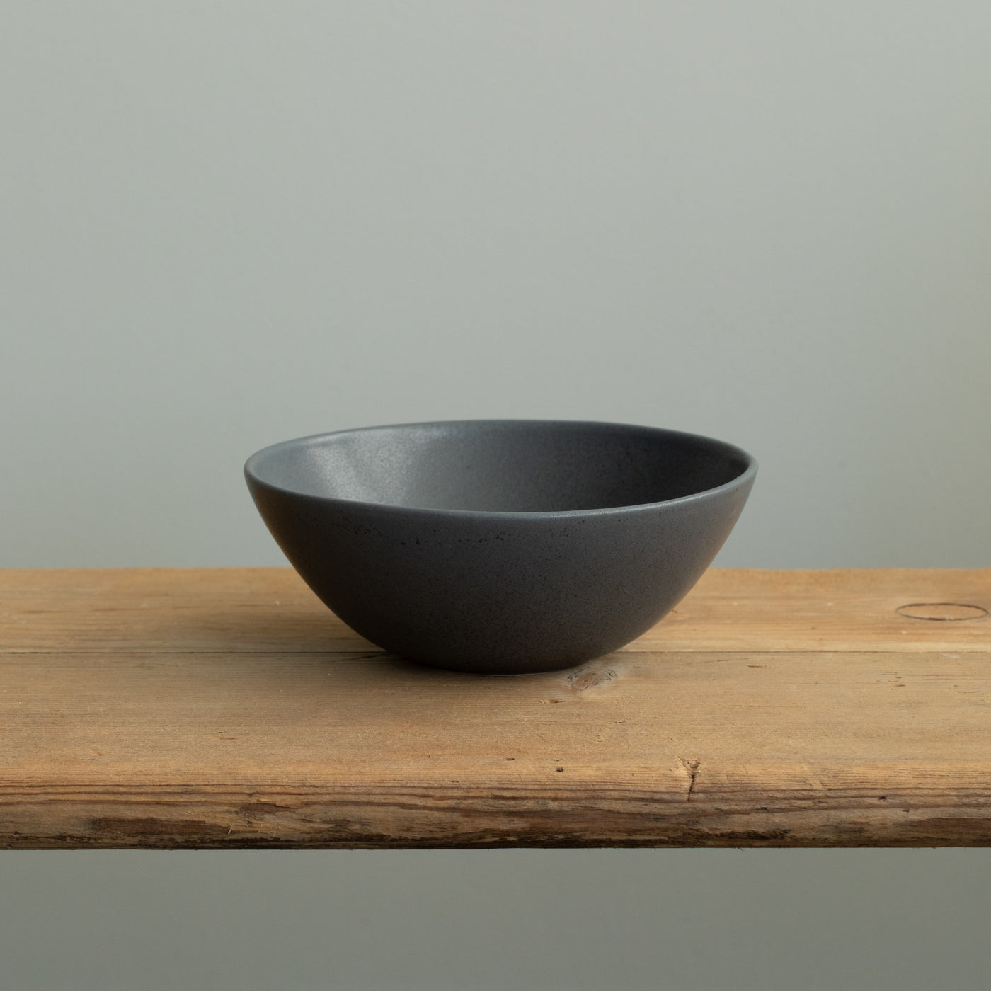 A matt black breakfast bowl with a rim slightly open towards the outside on a wooden table