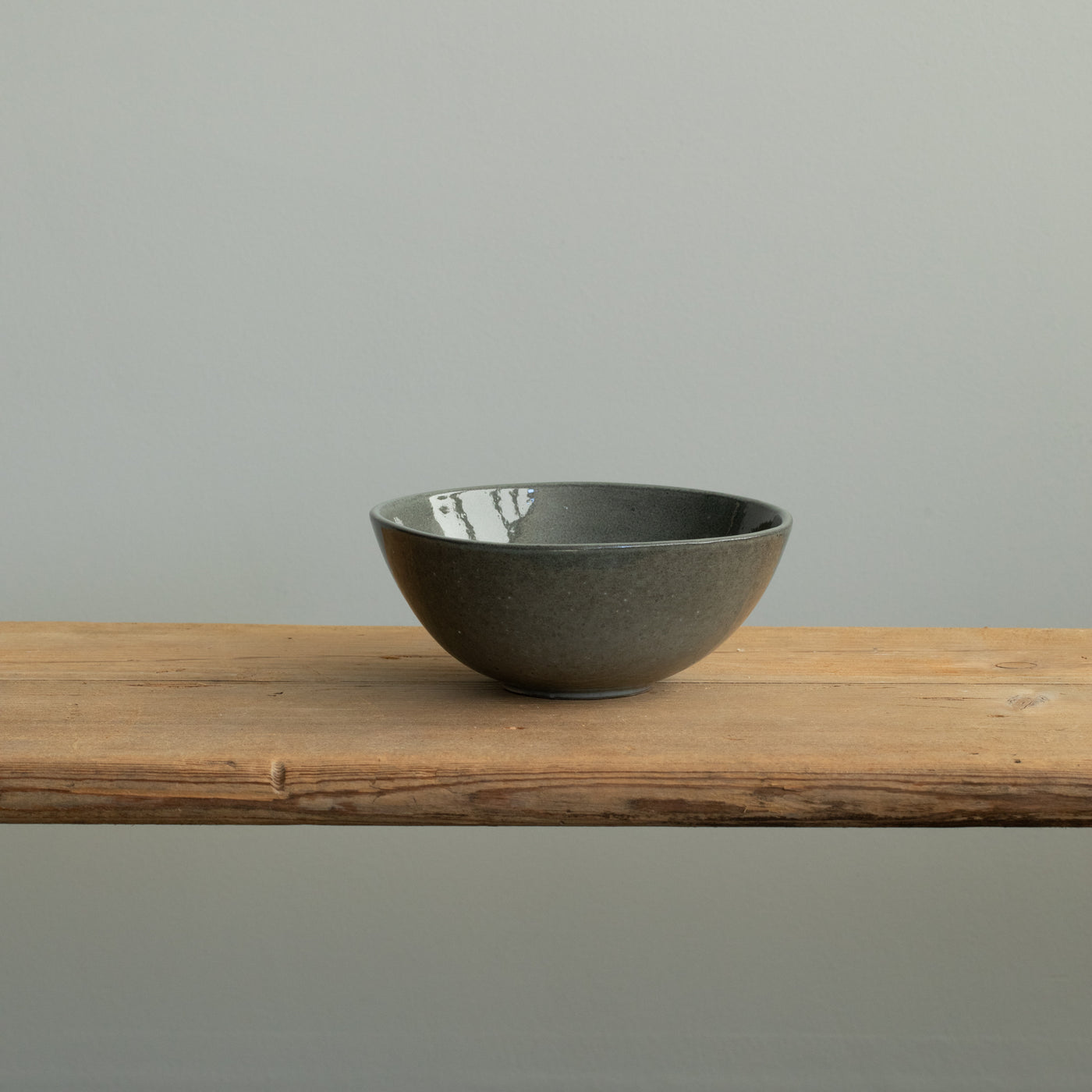 A shiny dark gray breakfast bowl with a slightly open rim on a wooden table