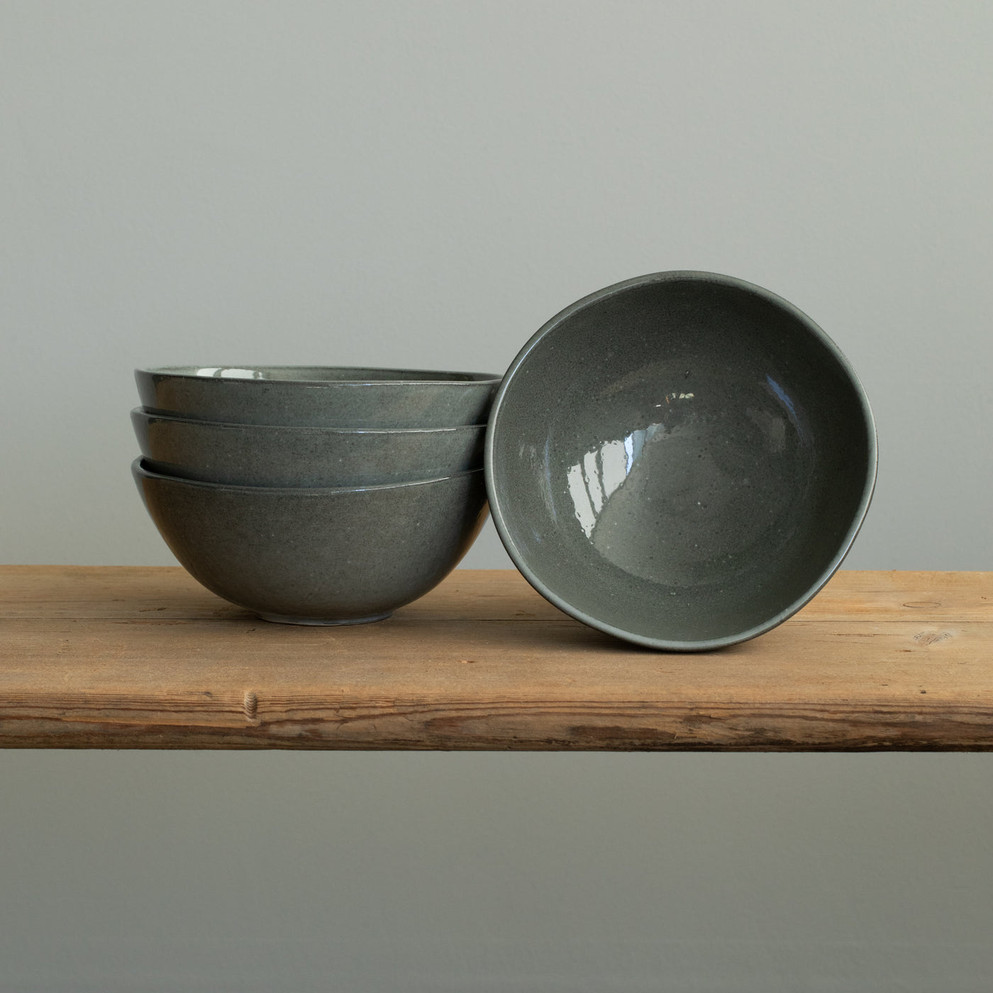 Three stacked dark gray muesli bowls and a small bowl placed on a wooden board