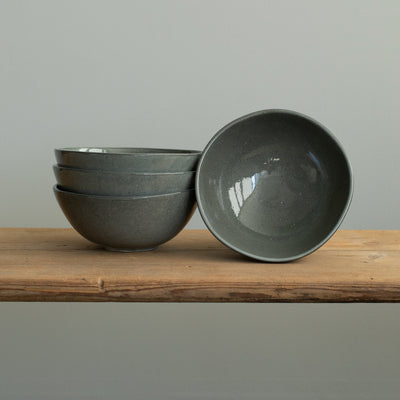 Three stacked dark gray muesli bowls and a small bowl placed on a wooden board