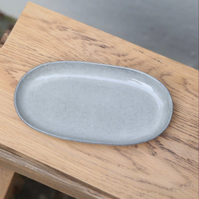 Light gray 22cm long oval saucer seen from above on a wooden board