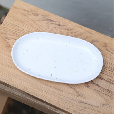 White oval saucer with white reactive glaze and golden dots