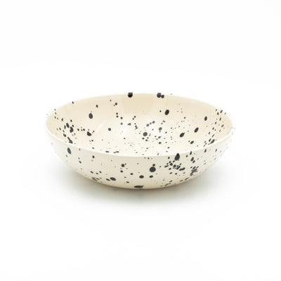 Round pasta plate in cream color with black splashes of paint against a white background
