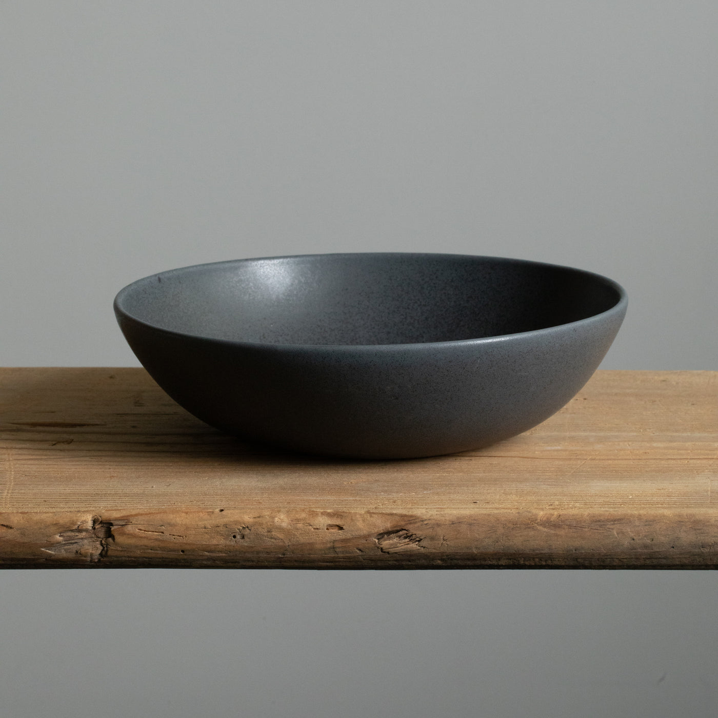 Matt black deep pasta plate seen from the front on a wooden table