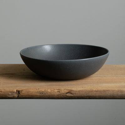 Matt black deep pasta plate seen from the front on a wooden table