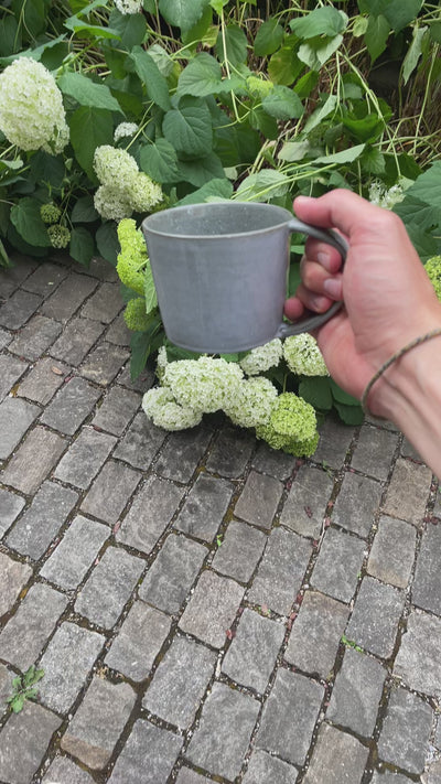 Large tea cup with handle is turned in all directions in daylight so that the gray-blue reactive glaze comes into its own