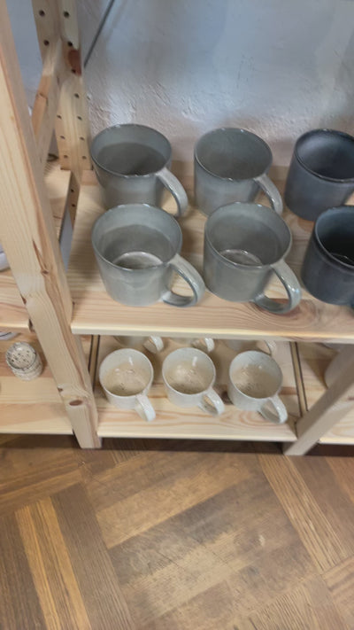 Large light gray teacup is taken from the shelf and turned in all directions so that the large round surface on the inside and the generous handle are shown to their best advantage