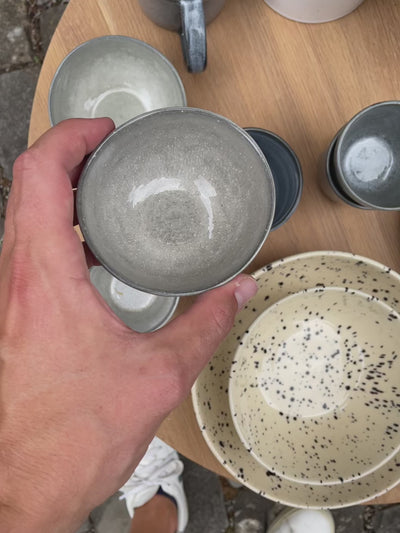 The small light gray snack bowl is shown from all sides. The bowl has an organic shape and a glossy Midnight Grey glaze.