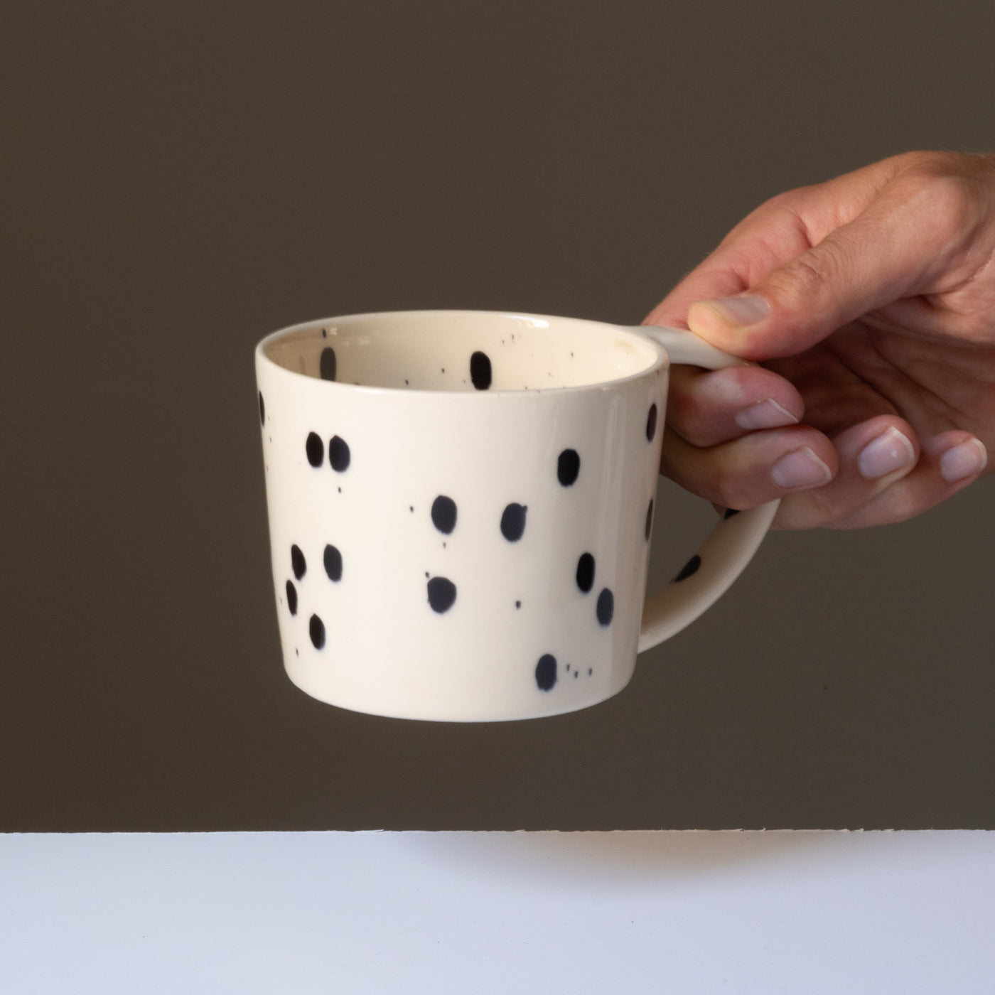 The cream-colored tea cup with black splashes of color is held by a hand on the large handle.