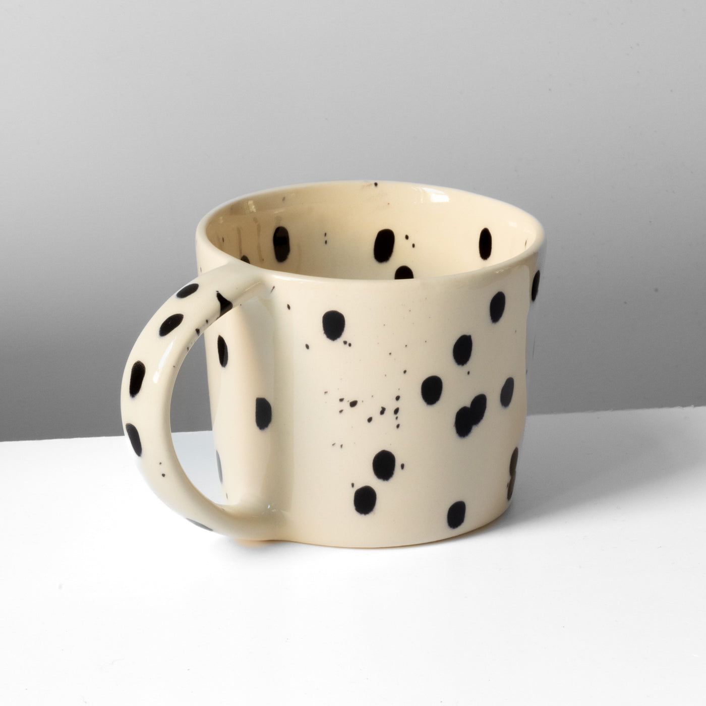 Large tea cup with handle in beige with black dots against a gray background