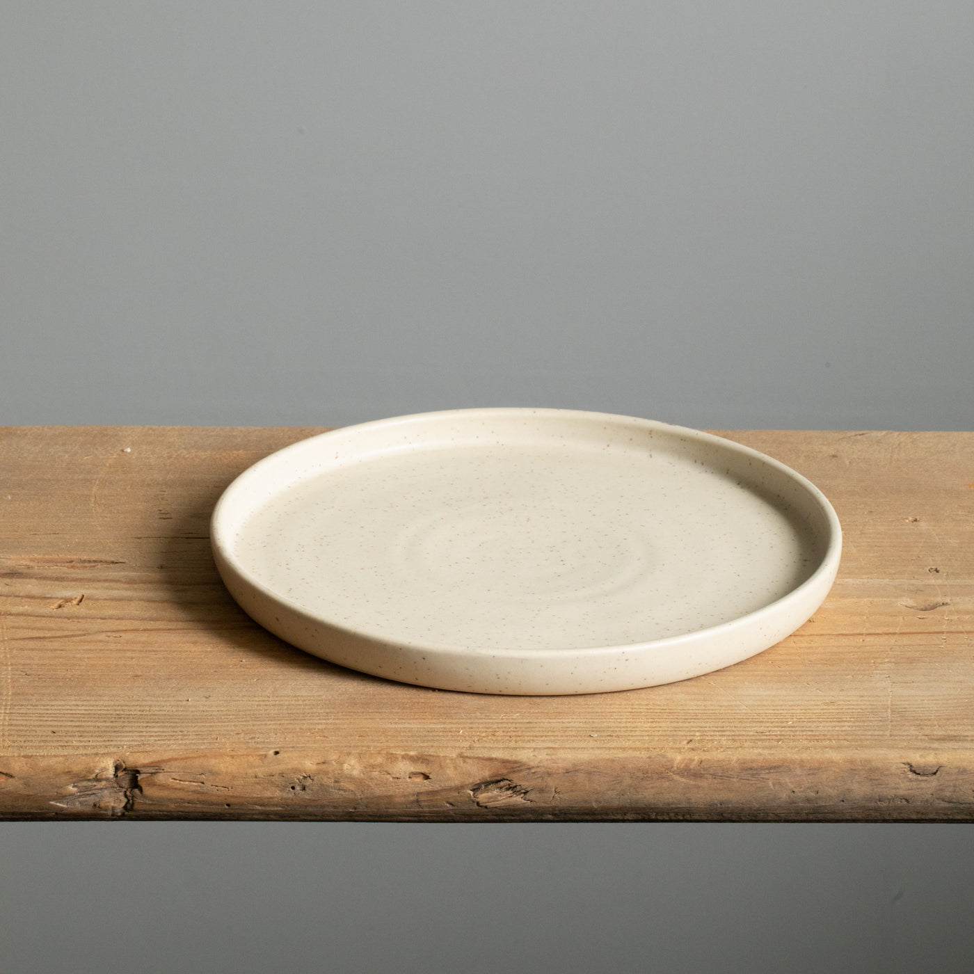 Beige small plate with straight rim and matt glaze lying on a wooden board