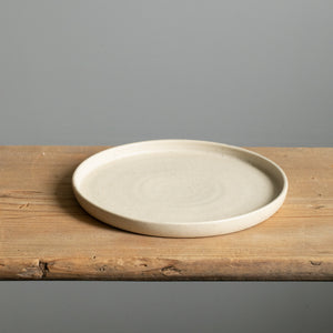 Beige small plate with straight rim and matt glaze lying on a wooden board