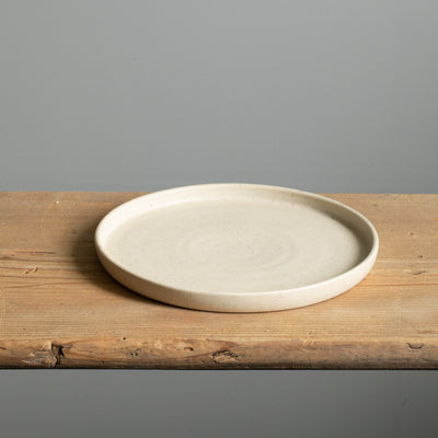 Beige small plate with straight rim and matt glaze lying on a wooden board