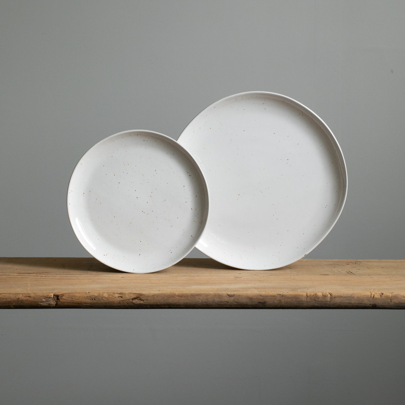 A small and a large stoneware plate placed next to each other in reactive white glaze with golden brown spots