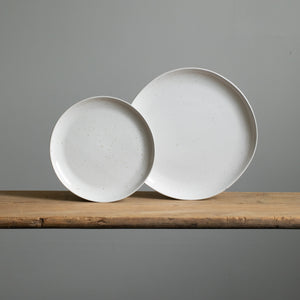 A small and a large stoneware plate placed next to each other in reactive white glaze with golden brown spots