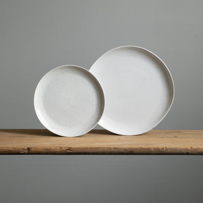 A small and a large stoneware plate placed next to each other in reactive white glaze with golden brown spots