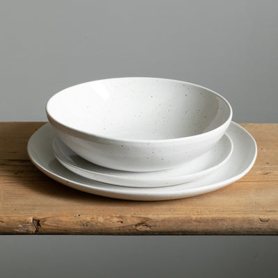 Large and small plates placed on top of each other and a white pasta plate with golden splashes of paint on top