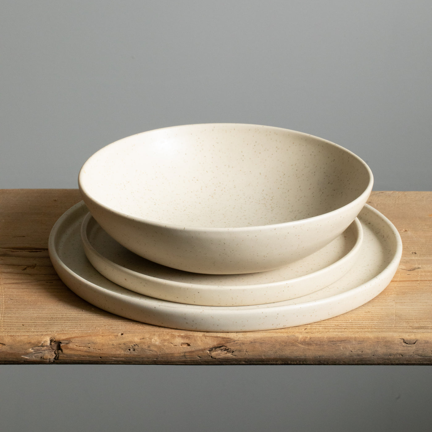 Large plate, small plate each with angled edge and a deep pasta plate all stacked in beige glaze.