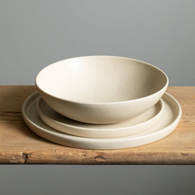 Large plate, small plate each with angled edge and a deep pasta plate all stacked in beige glaze.