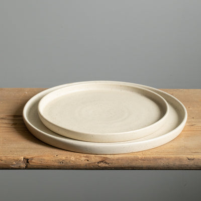 Large and small plate placed on top of each other with angled rim and matt beige glaze