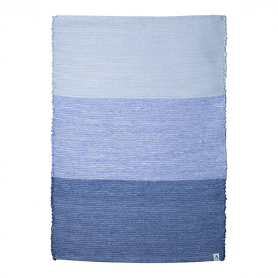 Hand-woven bathroom rug in 3 shades of blue set against a white background